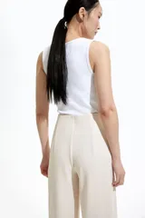 Pantalón de vestir color crema, de tiro alto y corte palazzo, con detalle de doble botonadura dorada en la parte superior.