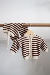 Conjunto tejido artesanalmente en hilado 70% algodón y 30% acrílico, compuesto por un cárdigan a rayas horizontales marrones y beige con botones y un pantalón a juego con cordón en la cintura.