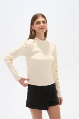 Sweater negro de punto con cuello alto y botones metálicos decorativos en hombros y mangas largas.