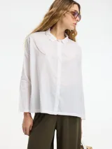 Camisa beige de algodón con botones frontales y cuello camisero.
