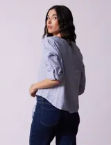Blusa de algodón a rayas verticales azules y blancas, con cuello en V, mangas 3/4 y cierre frontal con botones. Tiene un nudo en la parte delantera.