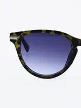 Lentes de sol con montura redonda de carey en tonos verde y marrón, con detalles metálicos plateados en los laterales. Los cristales son degradados en tonos azul y violeta.