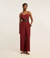 Mono de mujer color rojo oscuro (bordó), de corte recto y pierna ancha, con escote corazón y tirantes anchos con elástico. Presenta pliegues frontales que caen rectos hasta el ruedo.