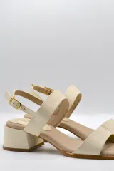 Sandalias de cuero color beige con taco cuadrado y tira ancha sobre los dedos. Presenta pulsera al tobillo con hebilla dorada.