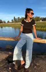 Remera negra de algodón con cuello redondo y mangas cortas. Presenta flores de crochet en tonos beige y blanco en el contorno del cuello y las mangas.