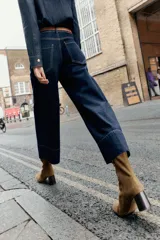 Botín de serraje color marrón, con tacón ancho en bloque y punta redonda. Presenta un detalle de pespunte en el cuerpo y cierre mediante cremallera lateral.