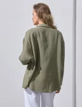 Camisa blanca de algodón con textura arrugada, cuello con solapa, abertura central con botones y bolsillo aplicado en el pecho. Mangas largas con largo regulable mediante presilla y botón.