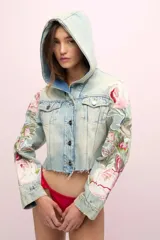 Campera de jean celeste con lavado gastado, corte cropped y capucha de jean. Presenta cierre frontal con botones metálicos, bolsillos delanteros y bordados florales en las mangas.