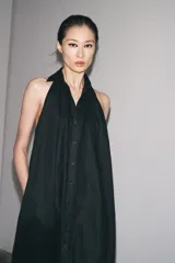 Vestido midi negro de lino, con cuello halter, hombros descubiertos, espalda descubierta, cierre frontal con botones y bajo asimétrico.