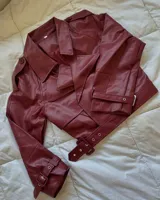 Campera corta de cuero sintético color borgoña, con cuello solapa, corte oversize, cierre cruzado con hebillas y cinturón.