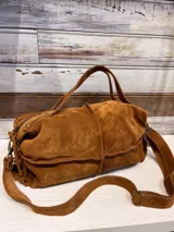 Bolso tipo bombonera color marrón chocolate, confeccionado en gamuza. Tiene doble asa corta y correa larga regulable y desmontable.