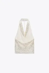 Top blanco con lentejuelas plateadas, de cuello halter y espalda descubierta.