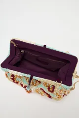 Bolso de mano tipo sobre con cuerpo cubierto de cuentas y abalorios en tonos celeste, beige, naranja y marrón. Tiene asa de cadena extraíble, bolsillo interior con cremallera y cierre con clip imantado y lazo.