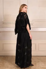 Camisa de encaje negra con escote en V, mangas amplias y cierre frontal con botones adornados con pines florales removibles en plateado y dorado.