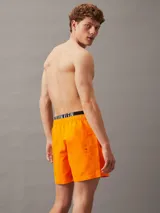 Short de baño naranja de poliéster reciclado, con cintura elástica negra con logo de Calvin Klein y cordón ajustable.