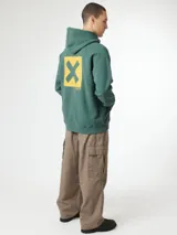 Buzo hoodie azul marino con capucha y cordones ajustables, de corte holgado y puños elásticos. Presenta un estampado en la espalda con una cruz dorada dentro de un cuadrado y texto en japonés.