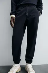 Pantalón jogger negro de corte slim fit, confeccionado en tejido de algodón con cintura elástica ajustable con cordón, bolsillos frontales y traseros de vivo, y bajo con puño elástico.