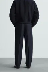 Pantalón de vestir negro, corte recto (straight fit), con cierre frontal de botón y cremallera. Presenta bolsillos delanteros, bolsillos traseros de vivo y un bolsillo de vivo adicional en la pernera.