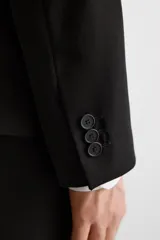Blazer slim fit negra confeccionada en tejido con viscosa. Cuello con solapas de muesca, manga larga con puño con detalle de botones, bolsillo de vivo en pecho y de solapa en cadera, bolsillo interior, bajo con aberturas en espalda y cierre frontal con botones.