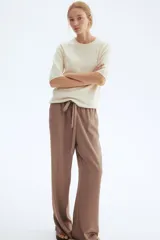 Remera de punto color crema, de corte holgado con hombros caídos y mangas cortas al codo. Presenta cuello redondo y remates acanalados en cuello, puños y bajo.