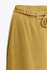 Pantalón ocre de algodón compacto, tiro medio, cintura elástica con cordón ajustable, pierna ancha y efecto lavado.