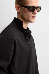 Polo de manga larga color negro, de punto tejido en hilatura de algodón, corte relaxed fit, con cuello solapa y cierre frontal de botonadura.