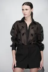 Camisa negra translúcida de organza con bordados de terciopelo en forma de labios, mangas abullonadas y cierre frontal con botones.