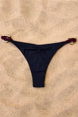 Bombacha de bikini color negro con textura acanalada y corte cavado. Presenta dos argollas doradas en los laterales unidas por tiras de tela color borgoña.
