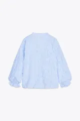 Blusa celeste con rayas verticales blancas, cuello redondo con escote en pico y mangas largas abullonadas terminadas en puño elástico. Presenta detalle de tejido en relieve con forma de flor.