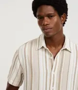 Camisa de manga corta para hombre marca Marfinno, confeccionada en tejido texturizado de mezcla de algodón y poliéster. Presenta un diseño de rayas verticales en tonos beige, gris y bordó, con cuello tradicional y cierre frontal mediante botones.