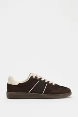 Zapatillas deportivas marrones con detalles en color crema y suela plana.