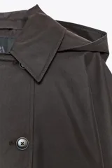 Trench corto color negro, con cuello solapa y capucha desmontable mediante botones. Manga larga tipo murciélago acabada en trabilla ajustable. Bolsillos laterales. Forro interior combinado. Cierre frontal con botones. Tejido repelente al agua.