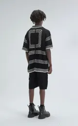 Camisa de manga corta color negro, tejida en punto abierto (símil crochet) con detalles en blanco. Tiene cuello tipo solapa, botones frontales y un calce oversize.