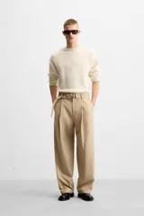 Pantalón negro de corte ancho con cinturón de tela con hebilla metálica y pliegues frontales.
