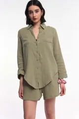 Camisa color verde oliva de corte clásico, con cuello camisero, cierre frontal con botones, mangas largas con puños abotonados, dos bolsillos de parche en el pecho y bajo redondeado.