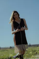 Vestido corto marrón de gamuza sintética, con escote en V y detalles bordados en blanco a lo largo del frente y los laterales. Presenta flecos en el ruedo.