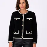 Saco negro de tejido bouclé con cuello redondo, cierre frontal con botones dorados con detalle de perlas, bolsillos frontales con solapa y ribete en contraste color crema.