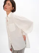 Camisa color blanco hueso de lyocell, holgada, con frunces en mangas y puño ancho. De largo por debajo de la cola y detalle de bordado del logo en espalda.