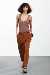 Pantalón color marrón confeccionado en hilatura con mezcla de lyocell y algodón. Tiro medio, cintura con trabillas, bolsillos laterales, pinzas en delantero y raya planchada. Cierre frontal con cremallera, botón y ganchos metálicos.
