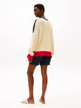 Cárdigan de punto color crema, con cuello en V, cierre con botones y corte amplio. Presenta detalles en azul marino en los hombros y en el borde del cuello, y detalles en rojo en los puños y en el ruedo. Logo de Tommy Hilfiger bordado en el pecho.