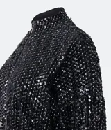 Campera bomber corta negra cubierta de lentejuelas metalizadas, con cuello alto, mangas largas, puños y bajo elásticos, y cierre frontal con cremallera.