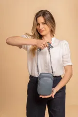 Bandolera pequeña tipo 'phone bag' de símil cuero color rosado pálido, con cierre de cremallera y correa ancha de tela con diseño de chevron en tonos claros.