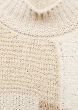 Sweater de punto grueso color beige con diseño patchwork. Tiene cuello alto y mangas largas.