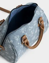 Cartera bowling de denim celeste con estampado de flores blancas, doble asa corta de cuero marrón y correa larga regulable y desmontable.