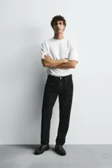 Jeans de denim de algodón, color negro lavado, con tiro medio, corte ajustado en cadera y muslos, y pierna que se estrecha hacia el tobillo. Presenta cinco bolsillos y cierre frontal con cremallera y botón.