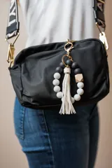 Llavero pulsera con cuentas redondas blancas y negras, cubo de madera y borla blanca.