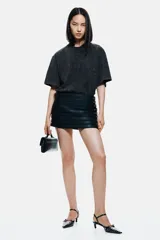 Remera de algodón con efecto acid wash en color negro o gris oscuro, corte oversize y cuello redondo acanalado con argollas metálicas decorativas.