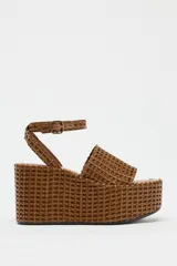 Sandalias con plataforma tipo cuña color marrón, con cuerpo trenzado, tira delantera y cierre mediante tira con hebilla a la pulsera del tobillo.