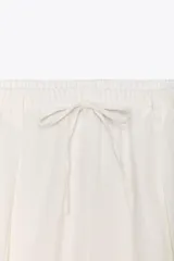 Pantalón blanco de lino, de corte ancho, tiro medio, con trabillas y cintura elástica ajustable con cordones.