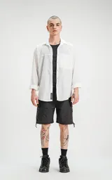 Camisa manga larga blanca de calce oversize con bolsillo con ojal y botón en delantero, confeccionada en textil plano fresco y liviano.